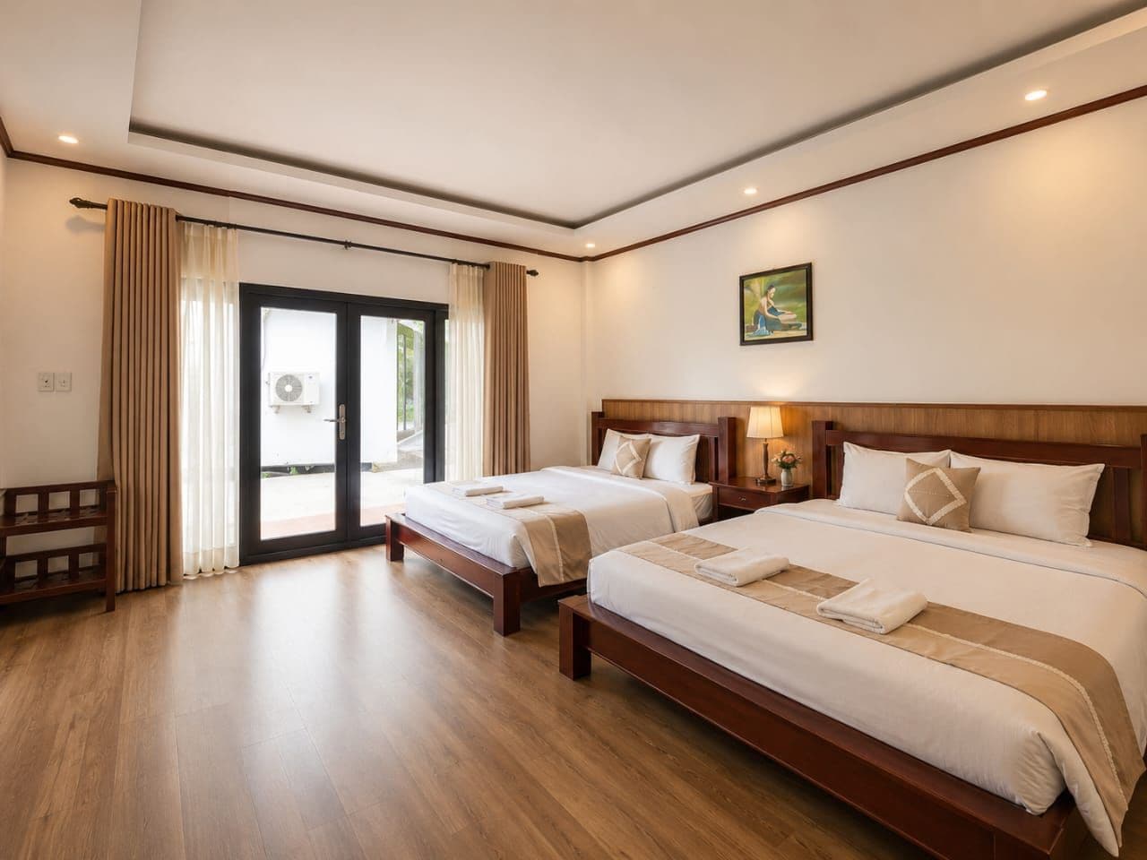 A hotel room with two beds, a wooden floor, a large window with curtains, and a painting on the wall.