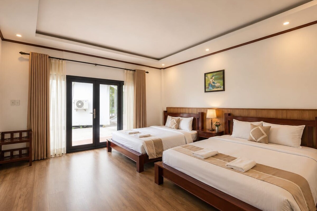 Habitación de hotel con dos camas, piso de madera, un ventanal con cortinas y un cuadro en la pared.