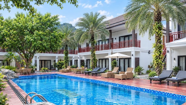 Una piscina con sillas de descanso y un edificio de dos pisos con balcones.