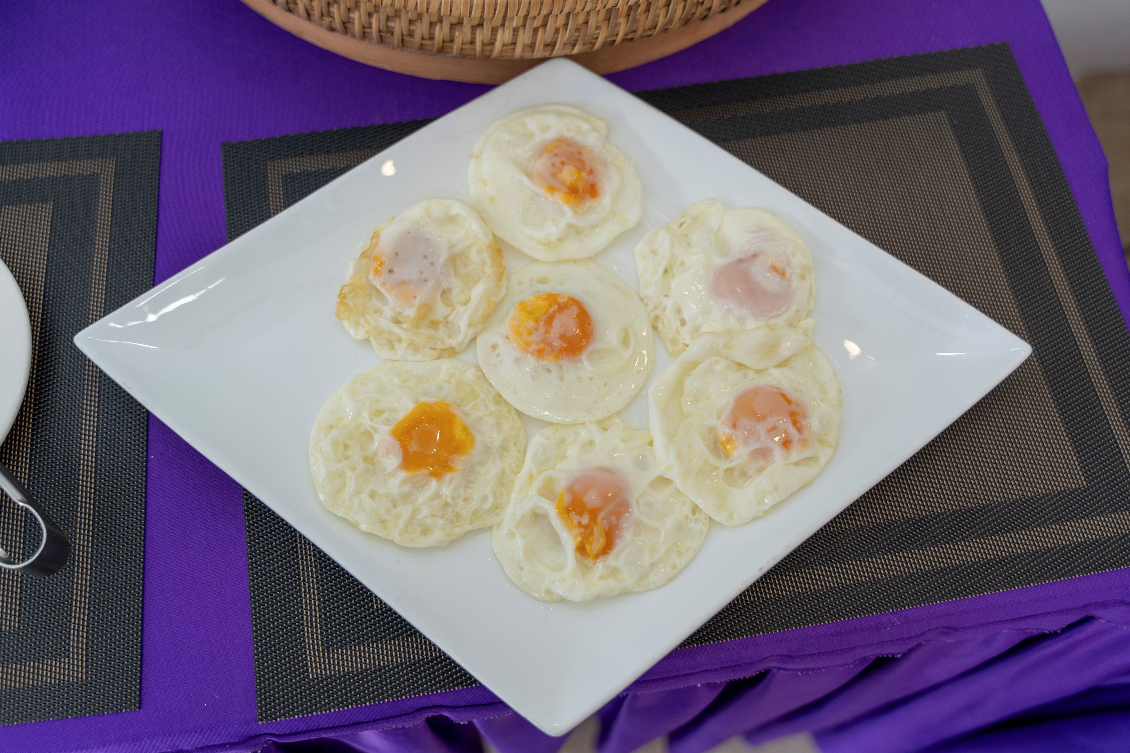 Une assiette blanche sur laquelle reposent six œufs au plat, le tout posé sur une nappe violette.