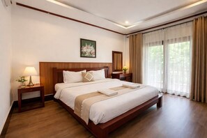 Ein Hotelzimmer mit einem großen Bett, einem Holzkopfstück, Nachttischen inklusive Lampen, einem Bild an der Wand und einem Fenster mit Vorhängen.