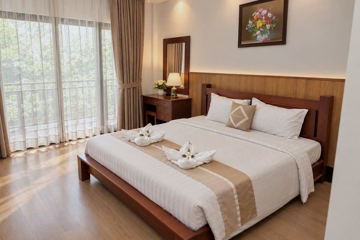 Habitación de hotel con una cama grande, cabecera de madera, una mesita de noche con lámpara y un cuadro en la pared.