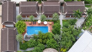 Un resort con piscina central, rodeado de exuberante vegetación y palmeras.