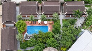 Un resort con piscina central, rodeado de exuberante vegetación y palmeras.