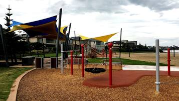 Kids can play on the slide and swings in this playground area surrounded by a mulch-covered ground and shaded by fabric canopies.
