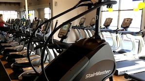 Rivi StairMaster-juoksumattoja kuntosalissa, jossa on puulattia ja suuret ikkunat.