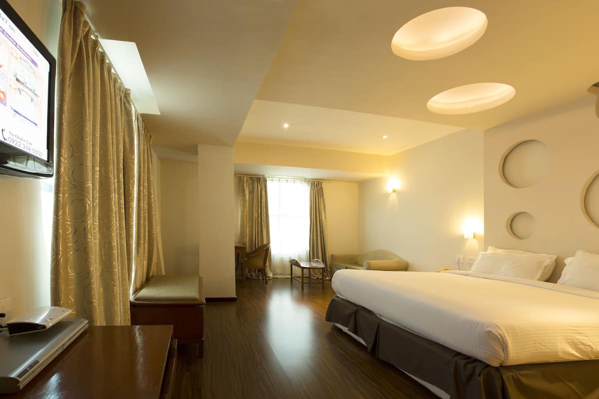 A hotel room with a large bed, a desk with a laptop, a chair, and a TV on the wall.