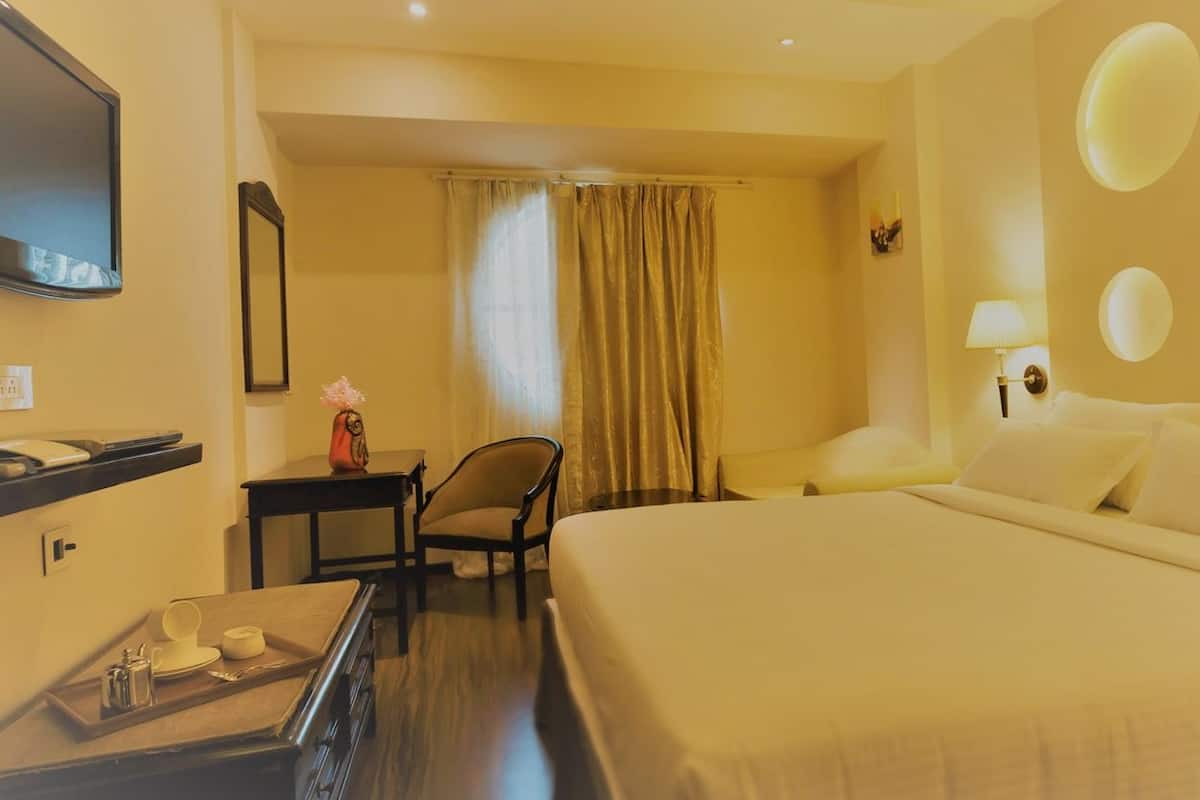 A hotel room with a large bed, a desk with a chair, a TV, and a window with curtains.