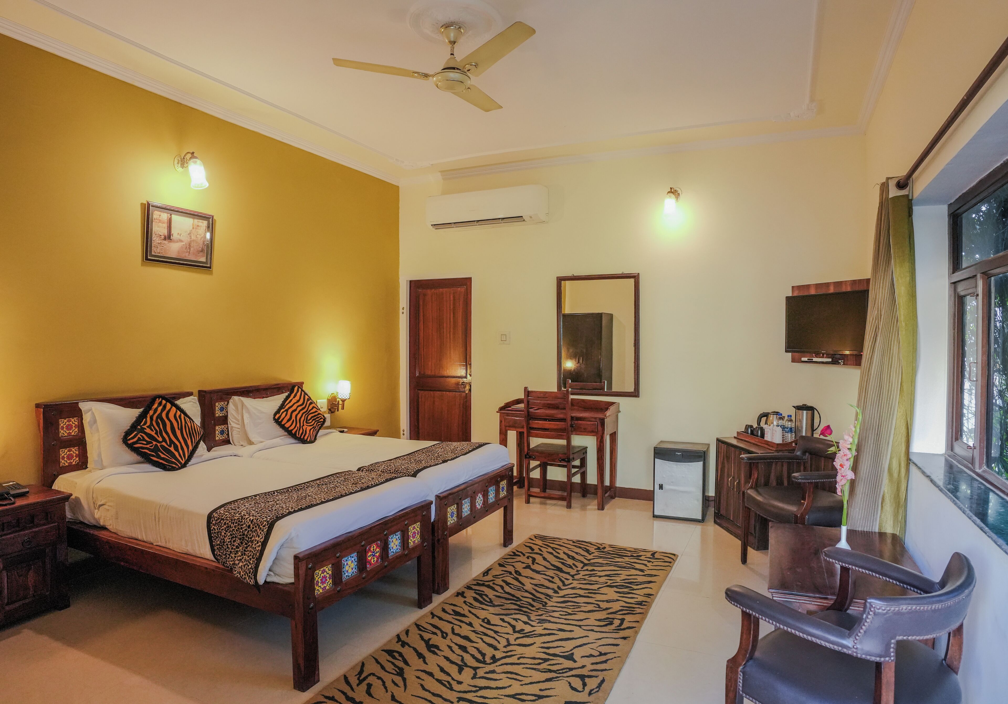 A hotel room with a bed, desk, chair, and a small table with a vase.