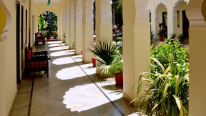 A corridor with arches, potted plants, and hanging lights. - Raj Palace Resort (Sawai Madhopur)