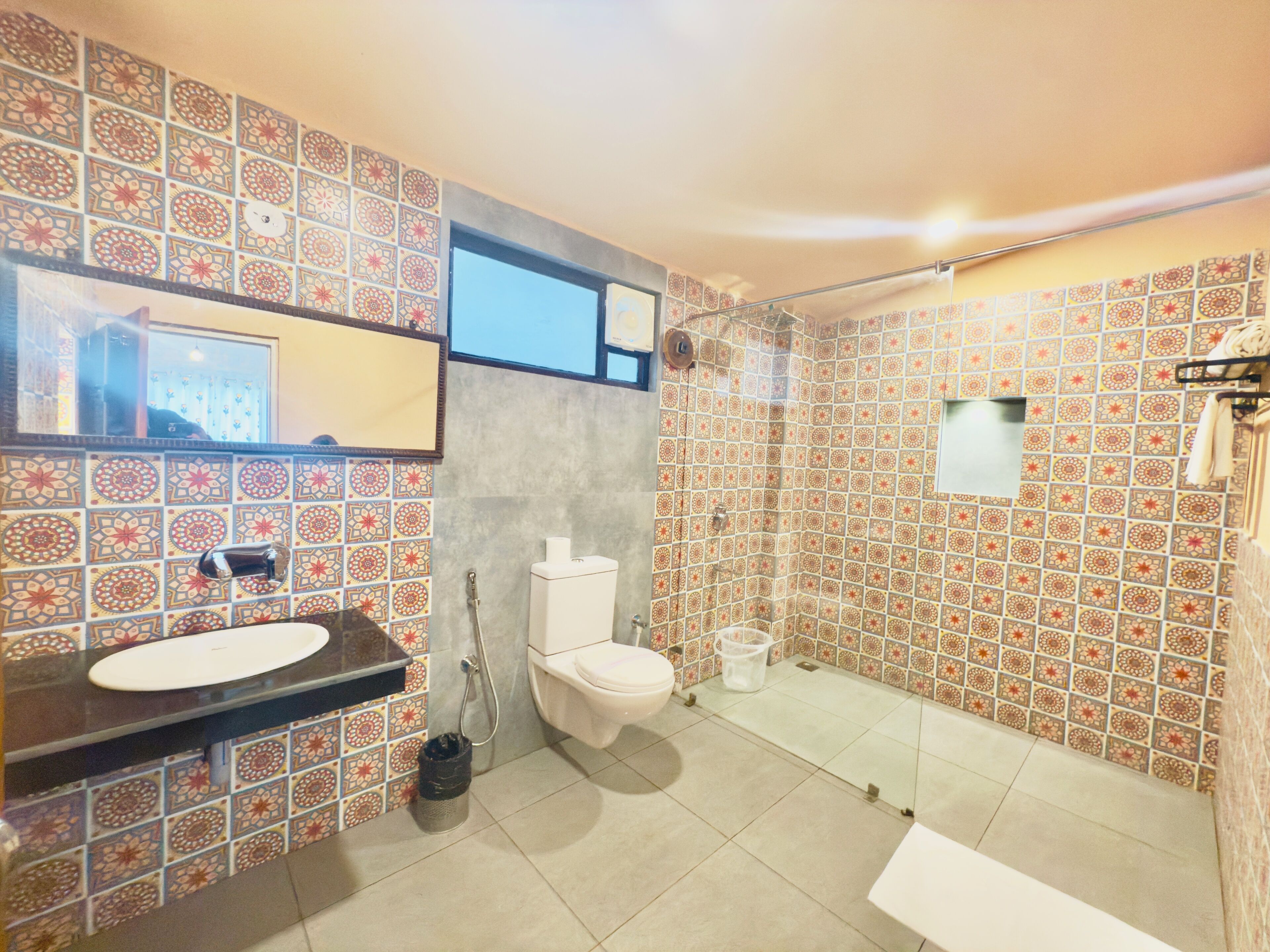 A bathroom with a sink, toilet, and shower area, featuring patterned tiles and a mirror.