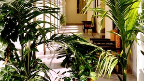 A corridor with a series of potted plants, a patterned ceiling, and a view into a room with a bed and a window. - Raj Palace Resort (Sawai Madhopur)