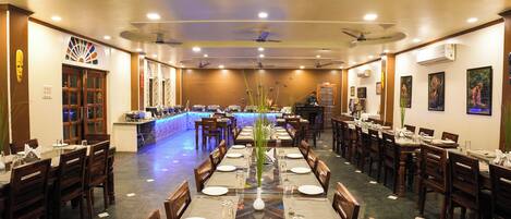 A restaurant with long tables, wooden chairs, and a bar area.