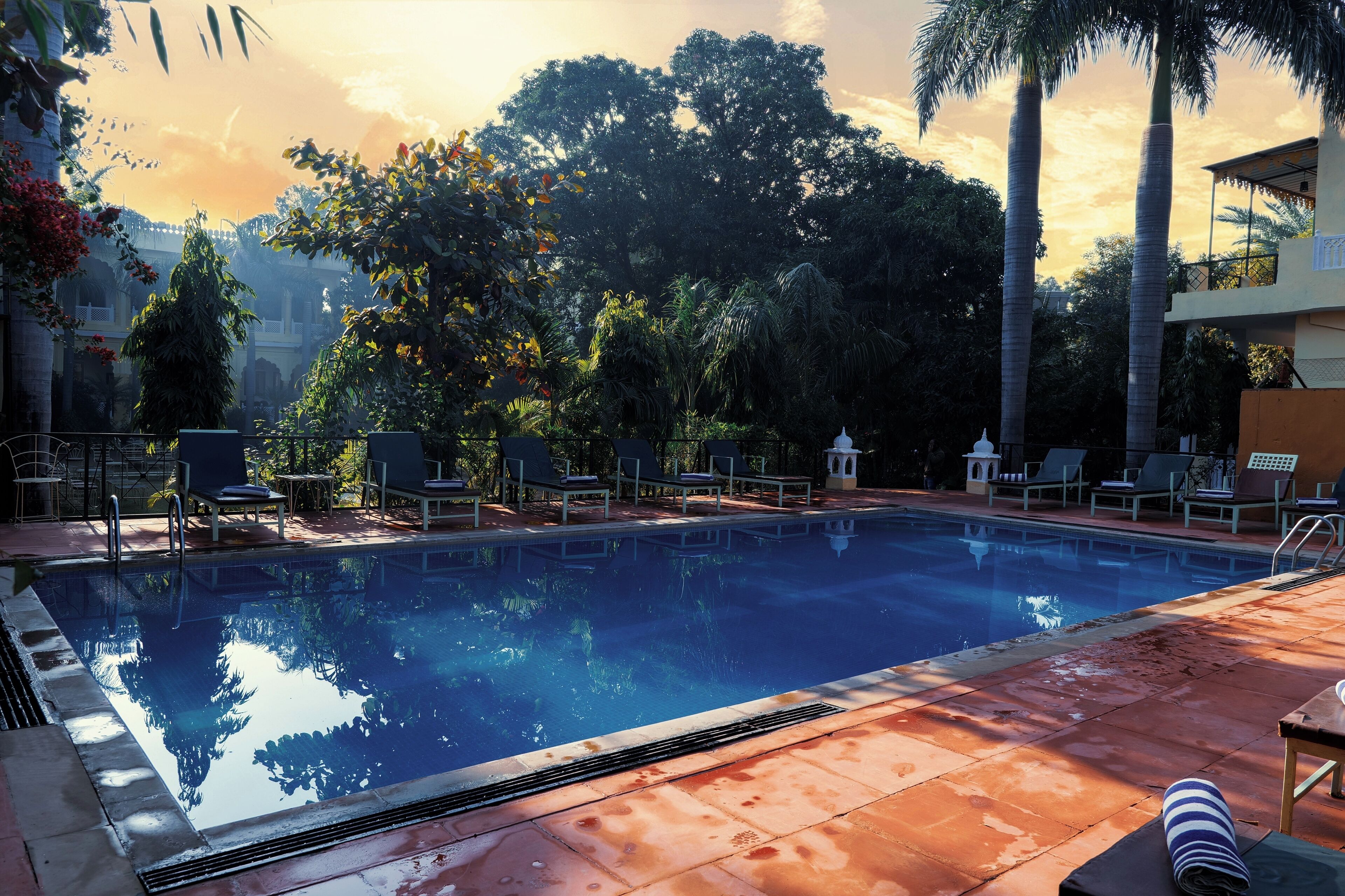A swimming pool with lounge chairs and a view of trees and a building in the background.