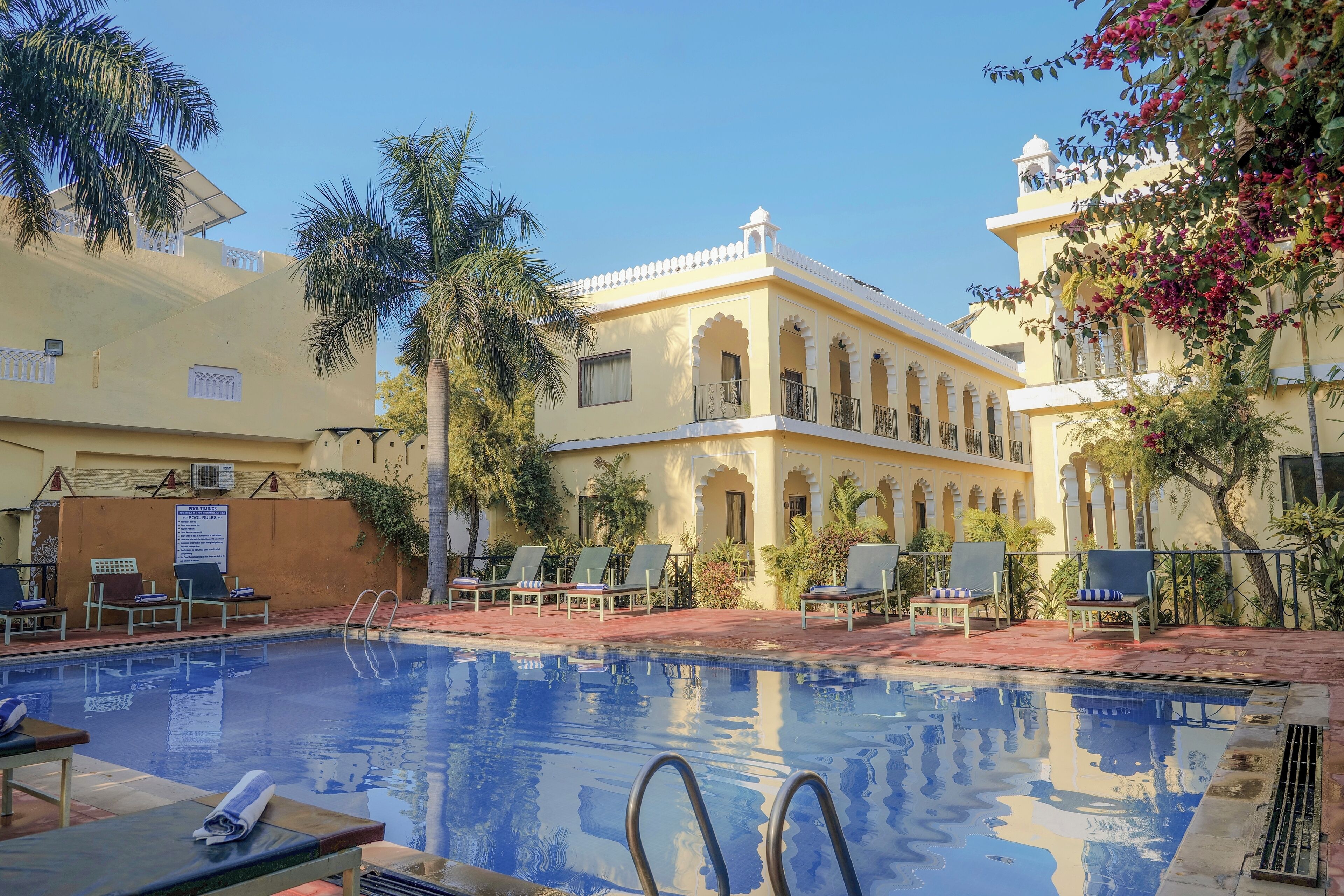 A pool area with lounge chairs and a building with arched windows and balconies.