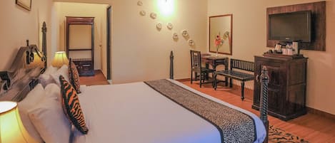 A hotel room with a large bed, a desk, a chair, a television, and a mirror.