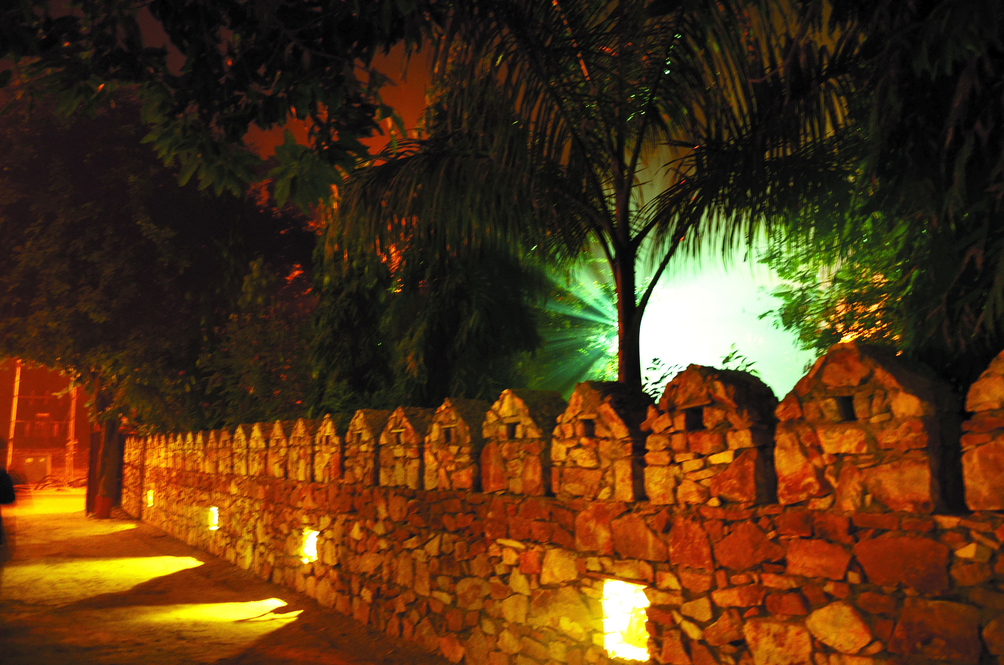 Muro de piedra con picos puntiagudos regularmente espaciados, posiblemente parte de un jardín o patio.