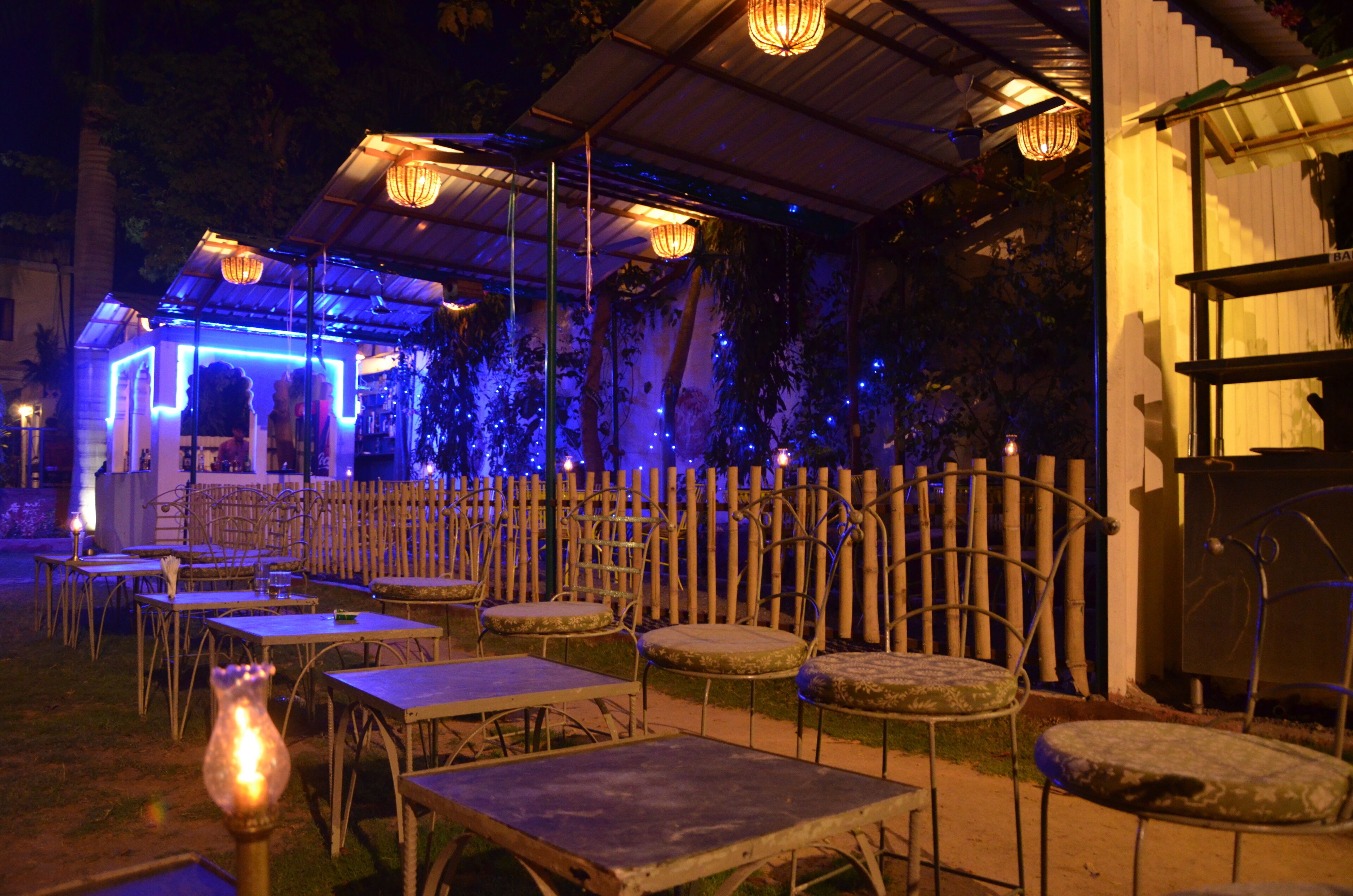 An outdoor dining area with tables and chairs, a wooden fence, and hanging lights.