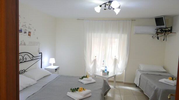 A hotel room with two beds, a desk, a chair, a TV on a stand, and a window with sheer curtains. - B&B Dimora Cirillo (Naples)
