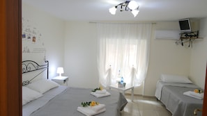 A hotel room with two beds, a desk, a chair, a TV on a stand, and a window with sheer curtains. - B&B Dimora Cirillo (Naples)