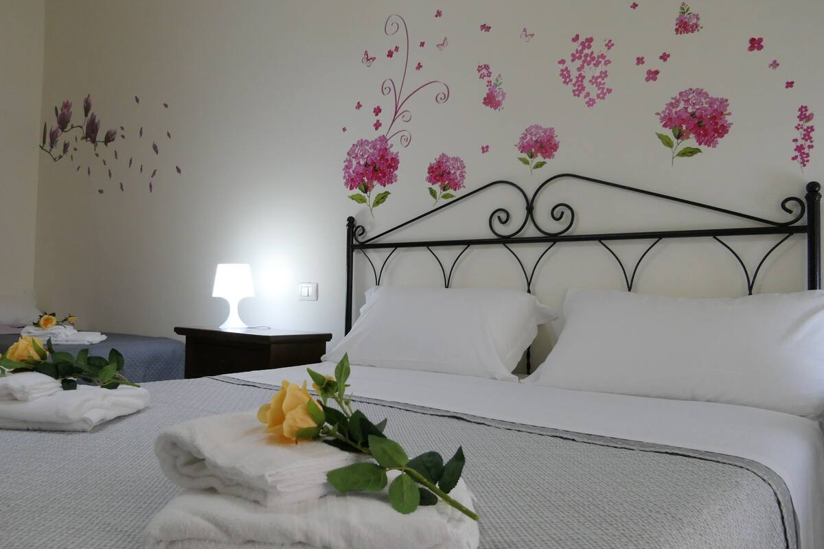 A hotel room with a neatly made bed, a bedside table with a lamp, and decorative wall art.