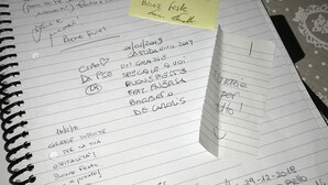 A notebook with handwritten notes and a sticky note on a table with a patterned tablecloth. - B&B Dimora Cirillo (Naples)