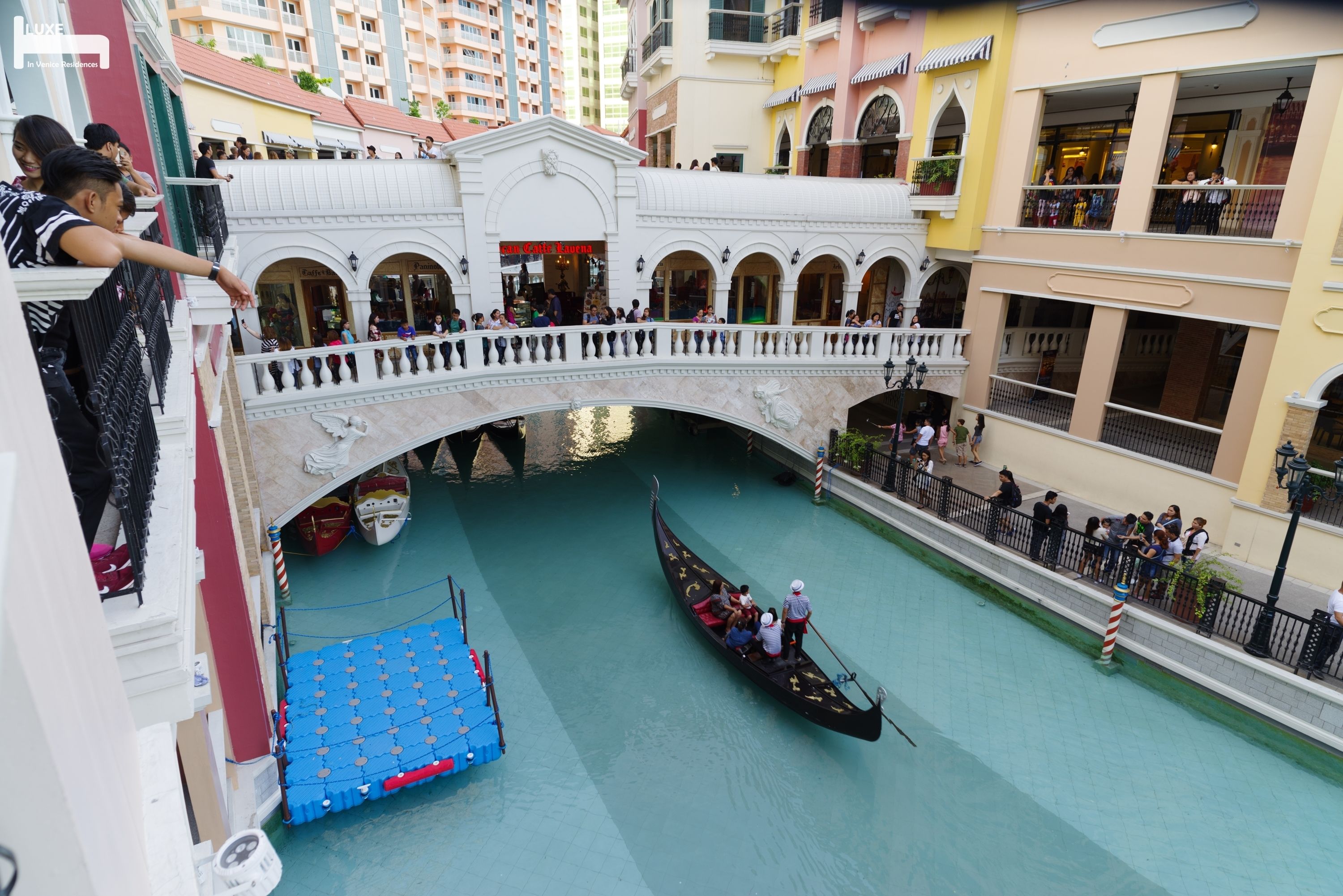 A gondola on a canal with a bridge overhead, surrounded by buildings with balconies and shops.