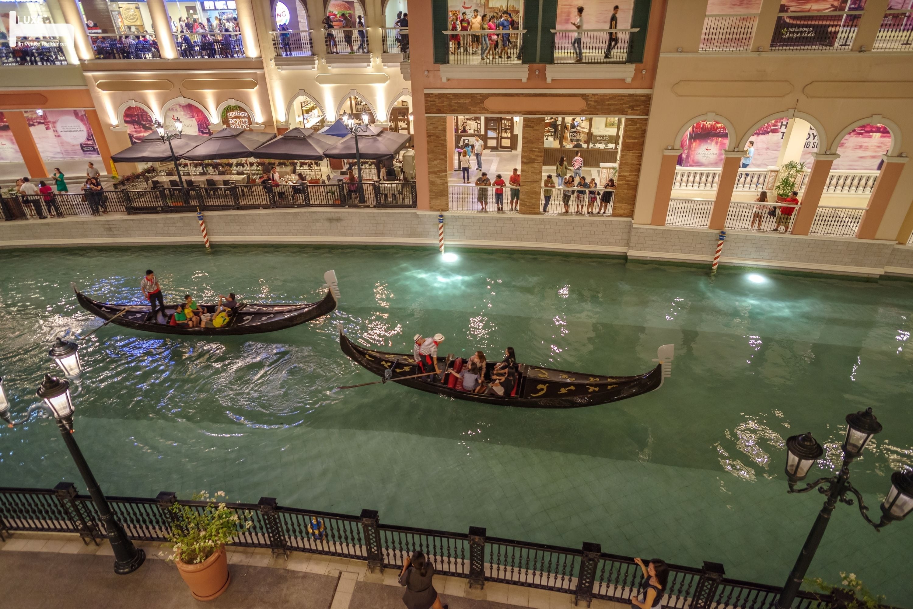 Ein großer, überdachter Wasserweg mit Gondeln, umgeben von einer hohen Halle mit Geschäften und Sitzbereichen.