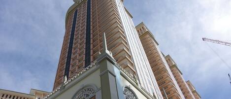 Um edifício alto com design arquitetônico moderno, com várias varandas e um elemento vertical marcante.