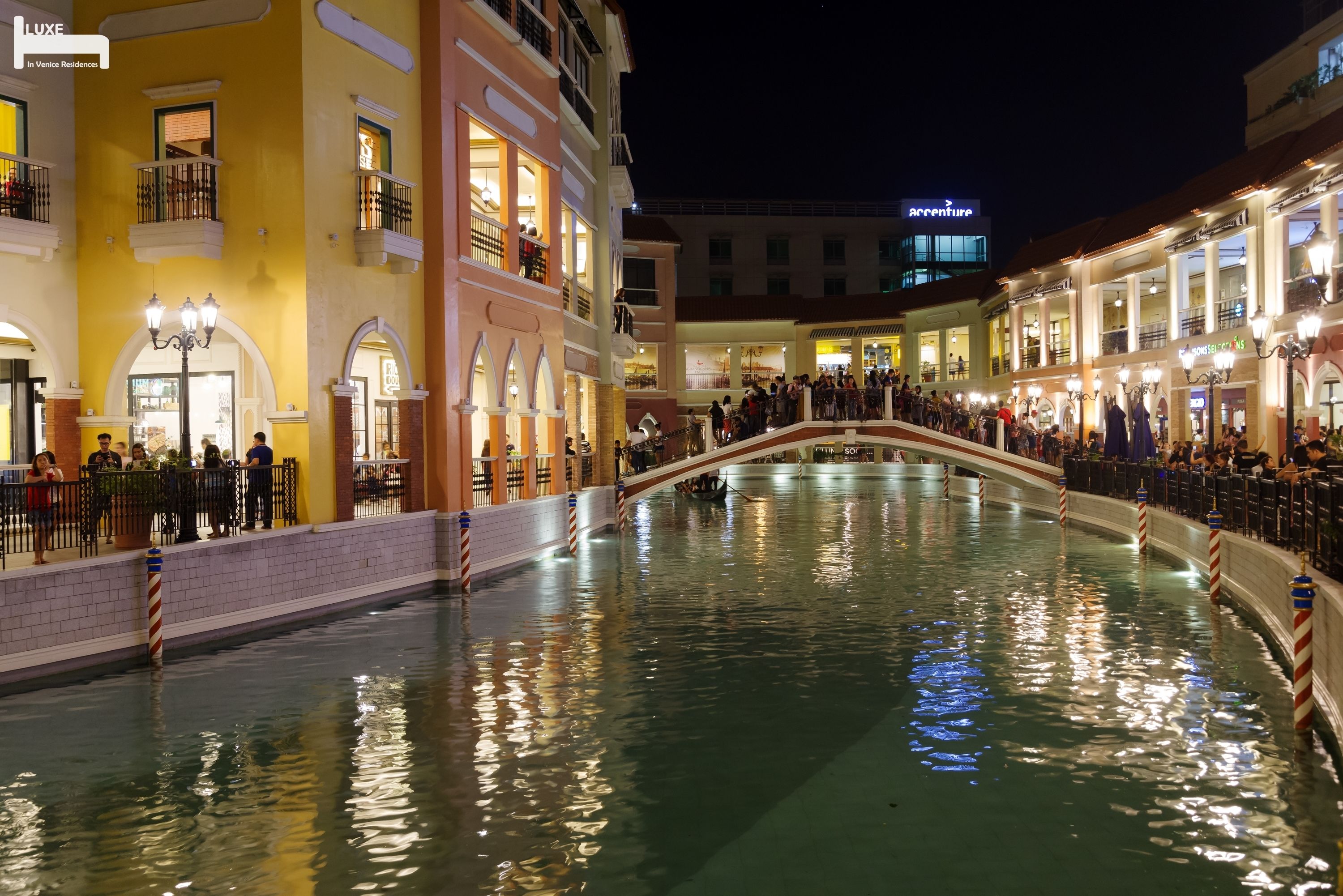 A canal with a pedestrian bridge in a brightly lit urban area.