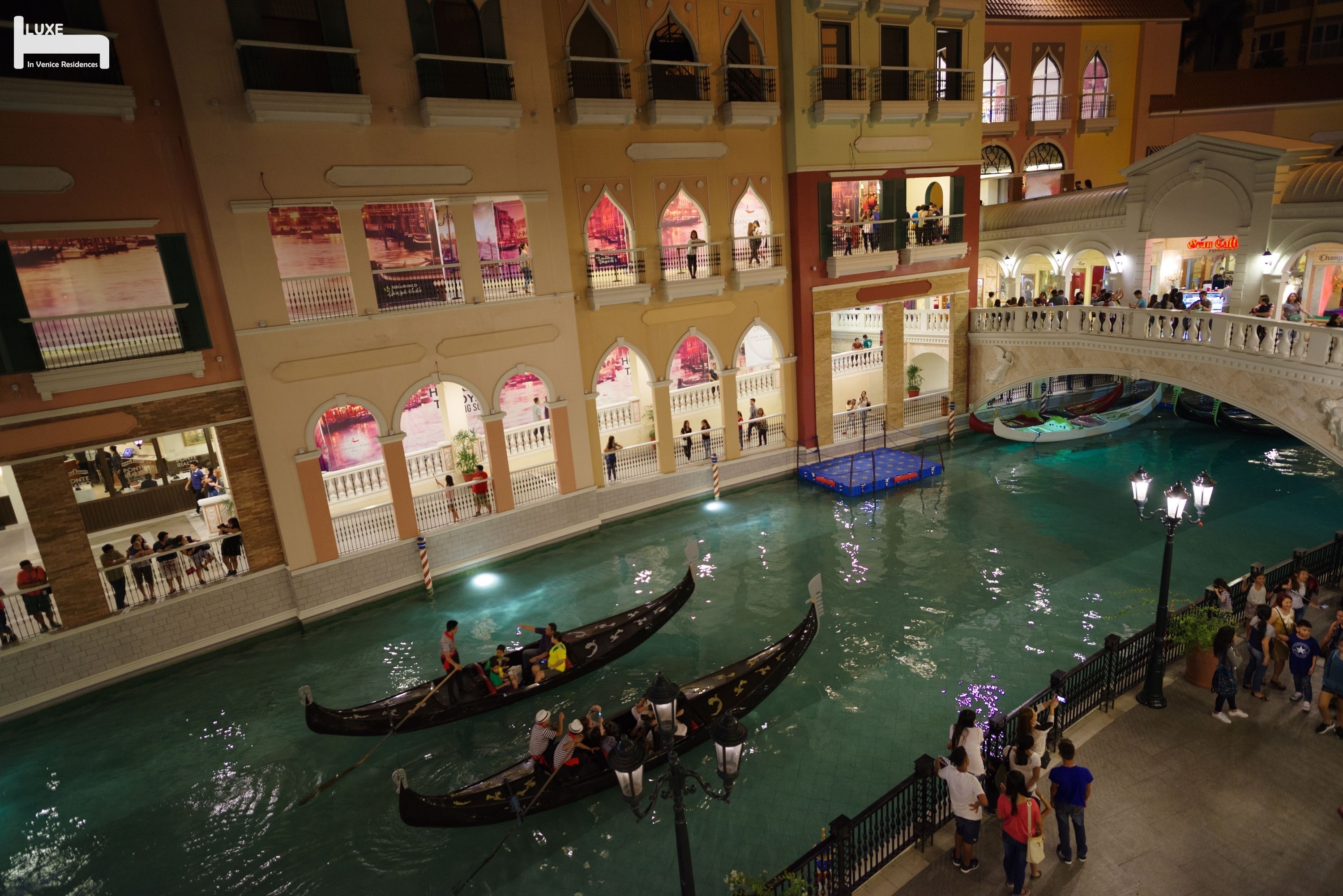 An indoor canal with gondolas, a bridge, and a crowd of people.