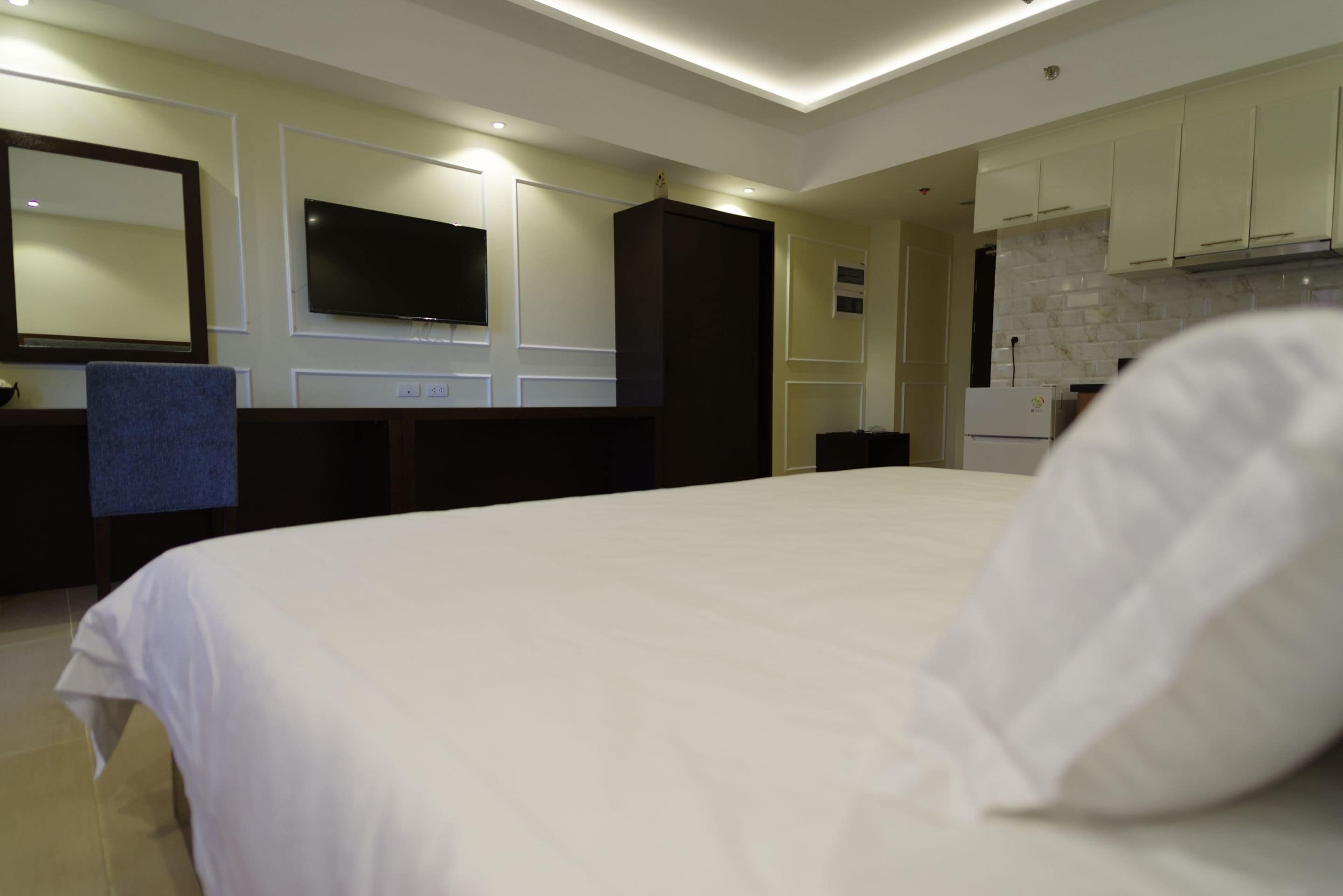 Een hotelkamer met een groot bed, een flatscreen televisie aan de muur, een kitchenette en een badkamer die door een open deur zichtbaar is.