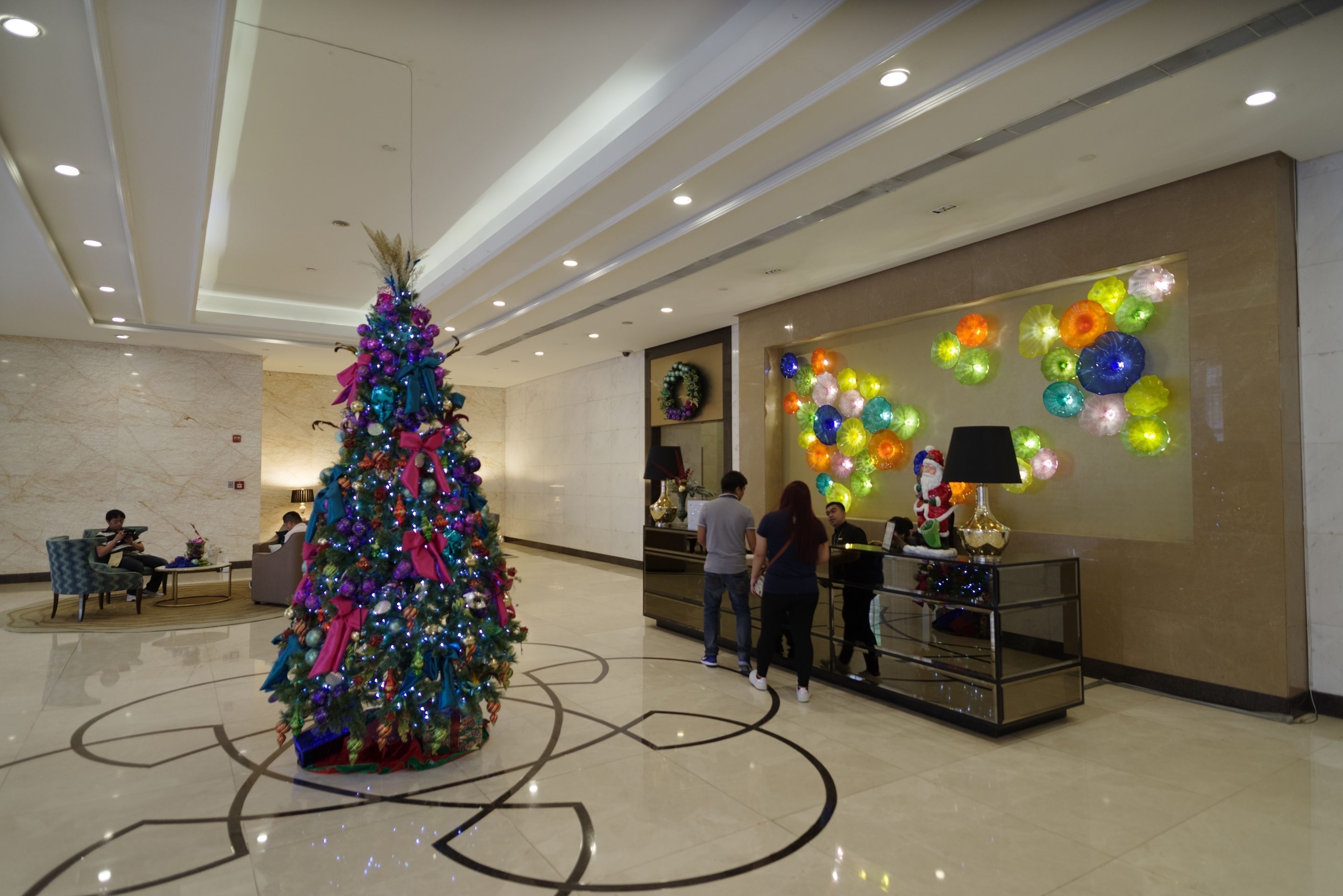 A lobby with a large Christmas tree, a reception desk, and colorful wall decorations.