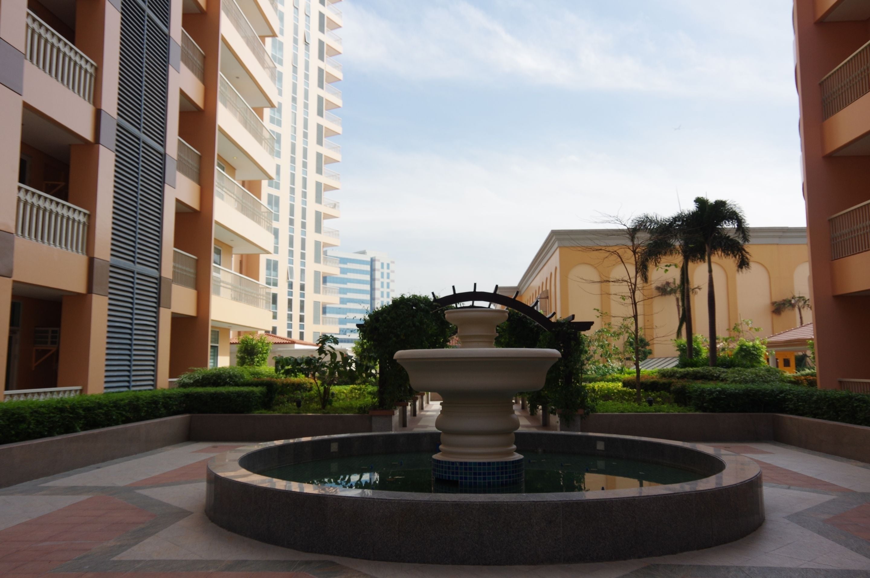 A courtyard with a central fountain, surrounded by greenery and modern buildings.