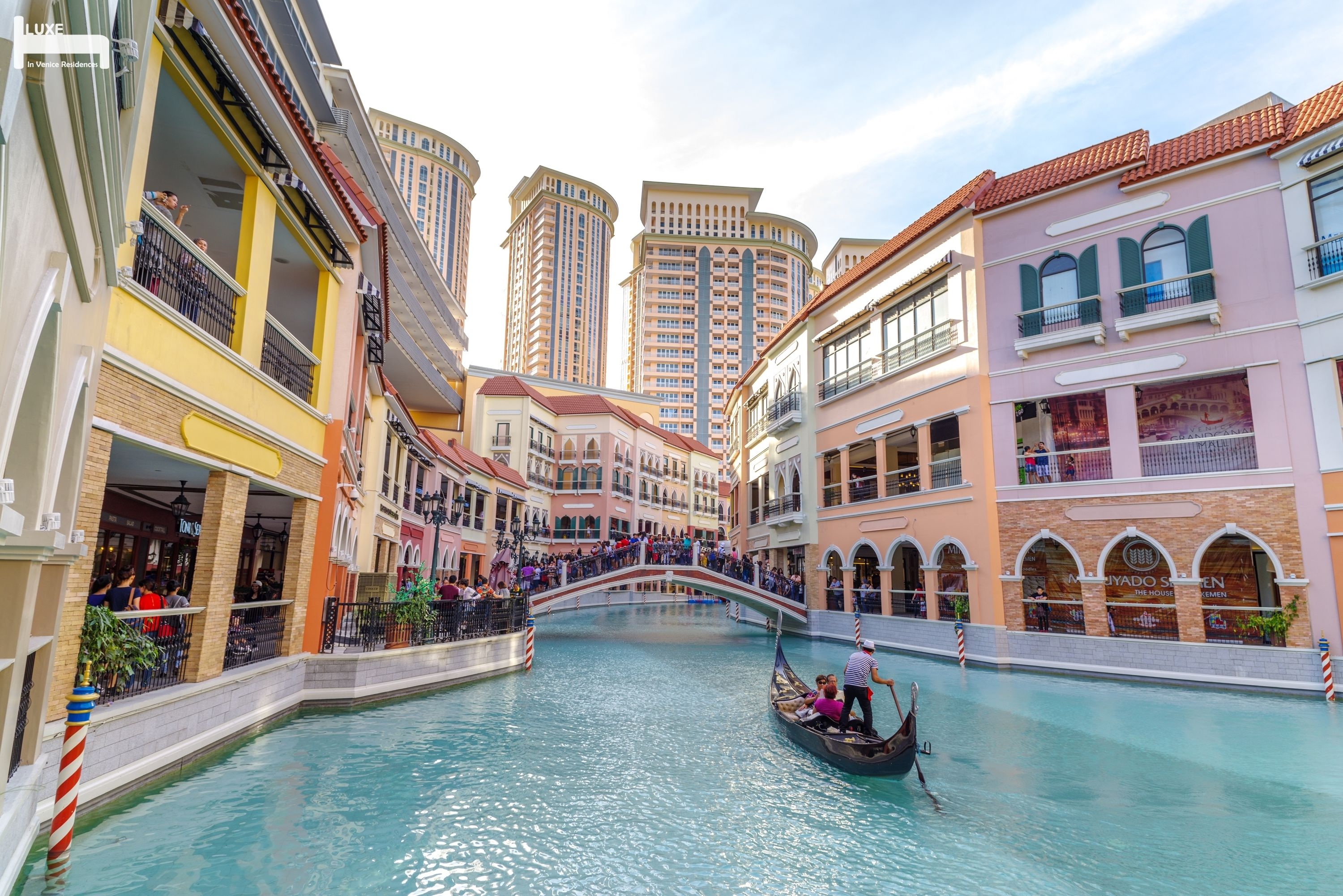 A canal with gondolas, a bridge, and high-rise buildings in the background.