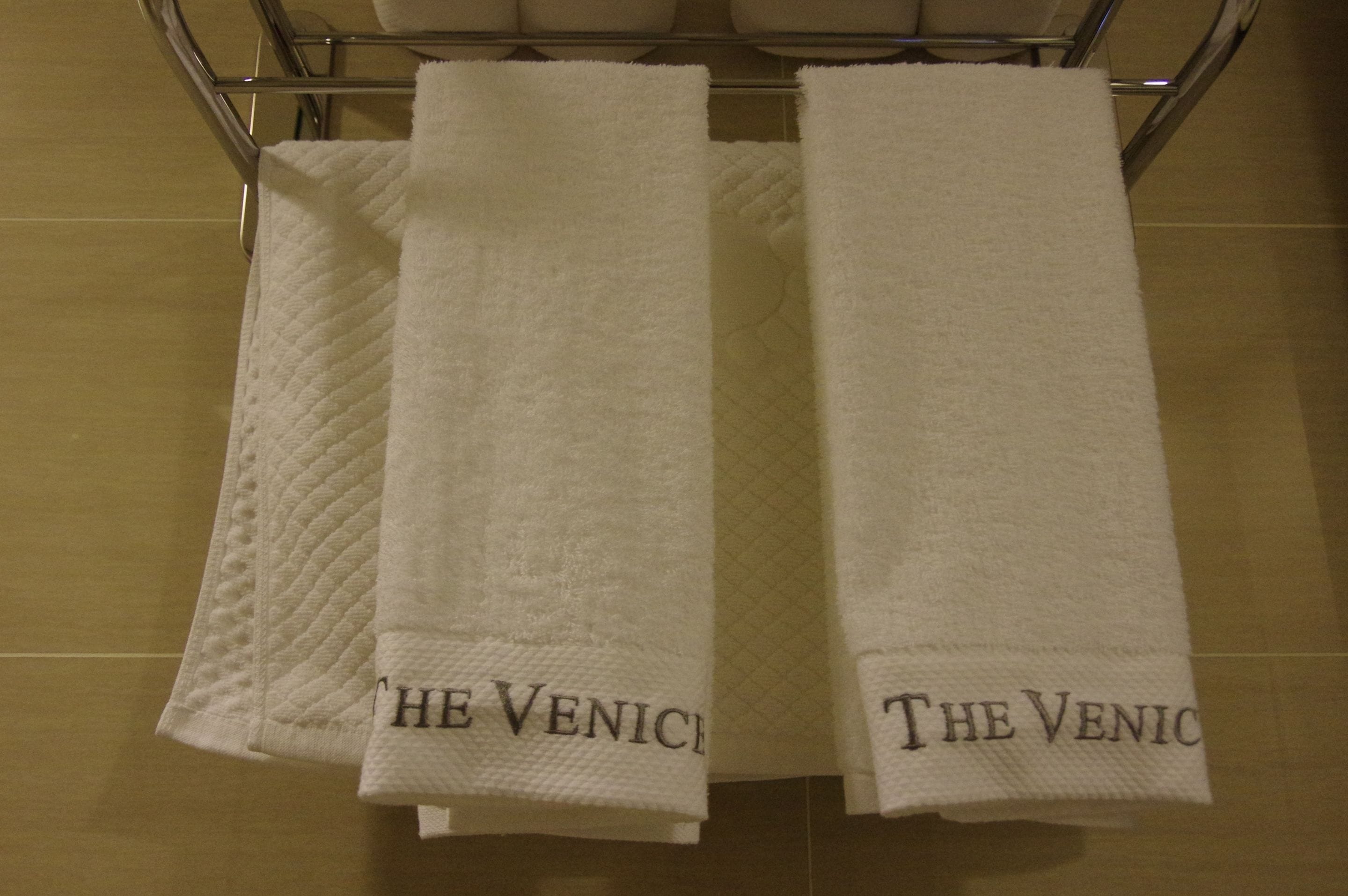 Two white towels with "The Venice" embroidered on them hanging on a metal rack.
