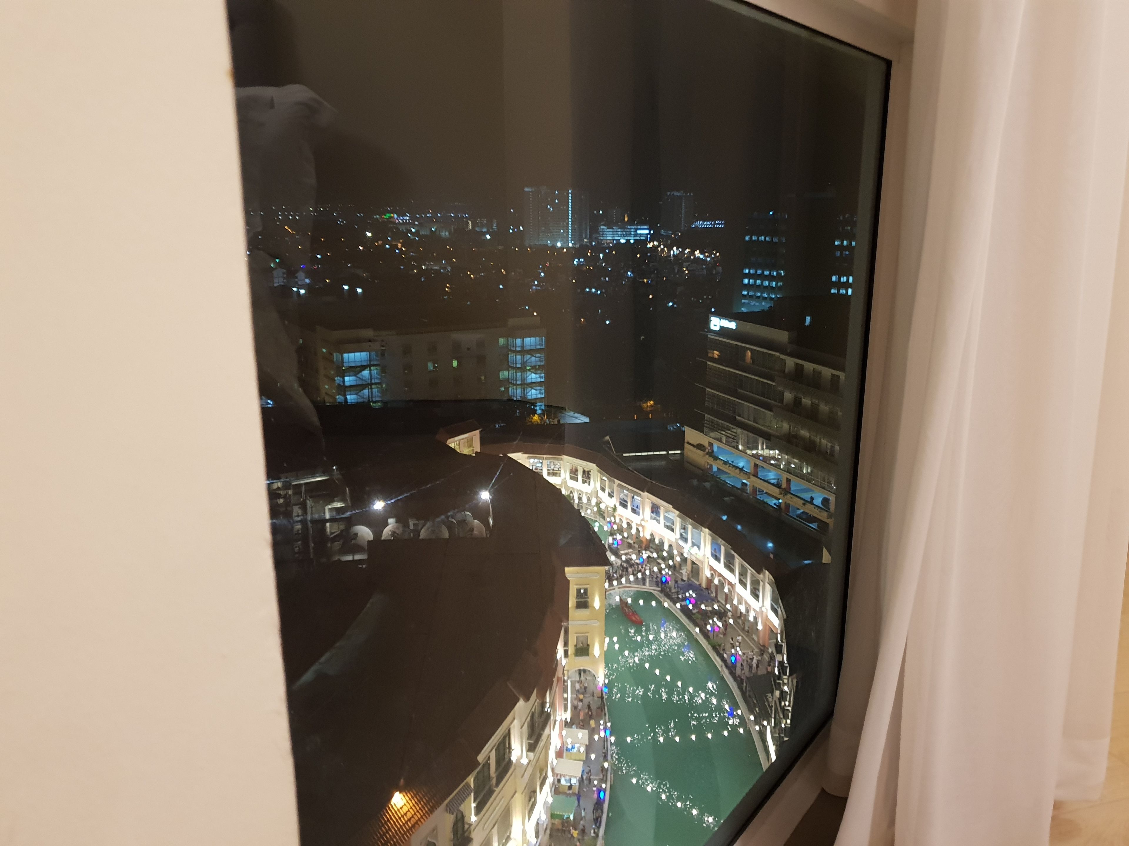 A nighttime view from a high-rise window overlooking a cityscape with illuminated buildings and a busy street below.