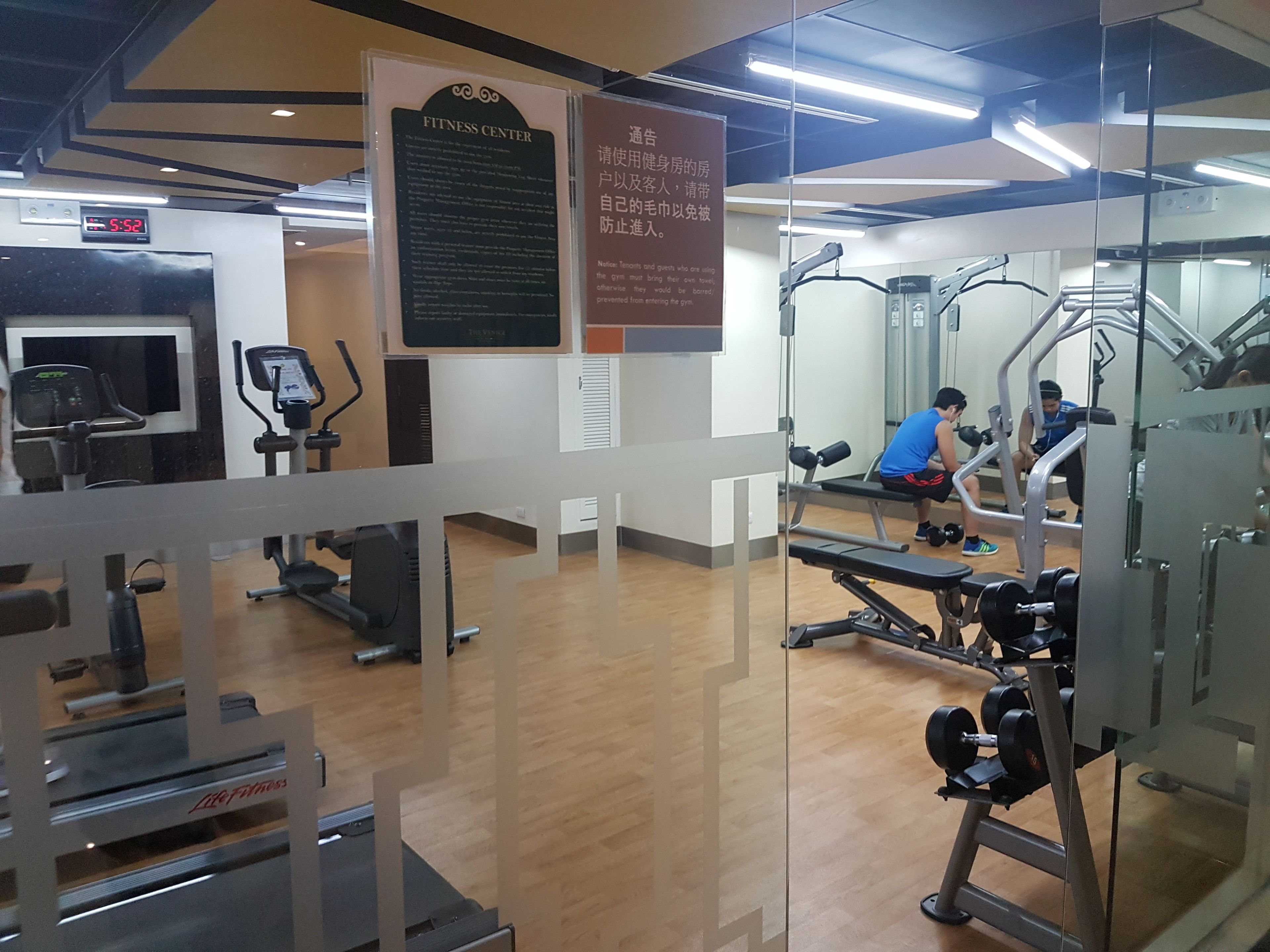 Een fitnessruimte met trainingsapparatuur, een digitale klok en informatieborden.