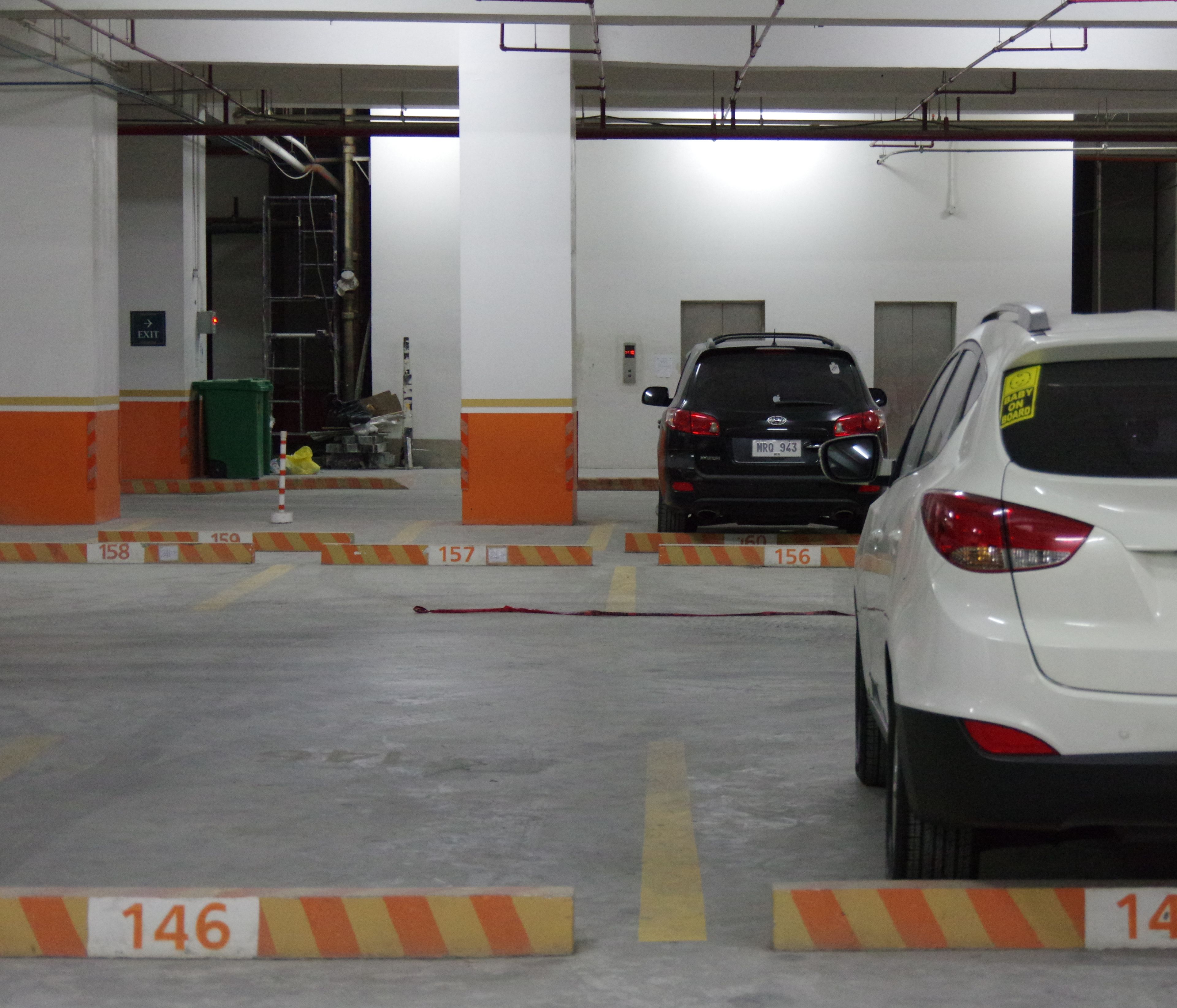 A parking garage with multiple levels, marked parking spaces, and a fire extinguisher on the wall.