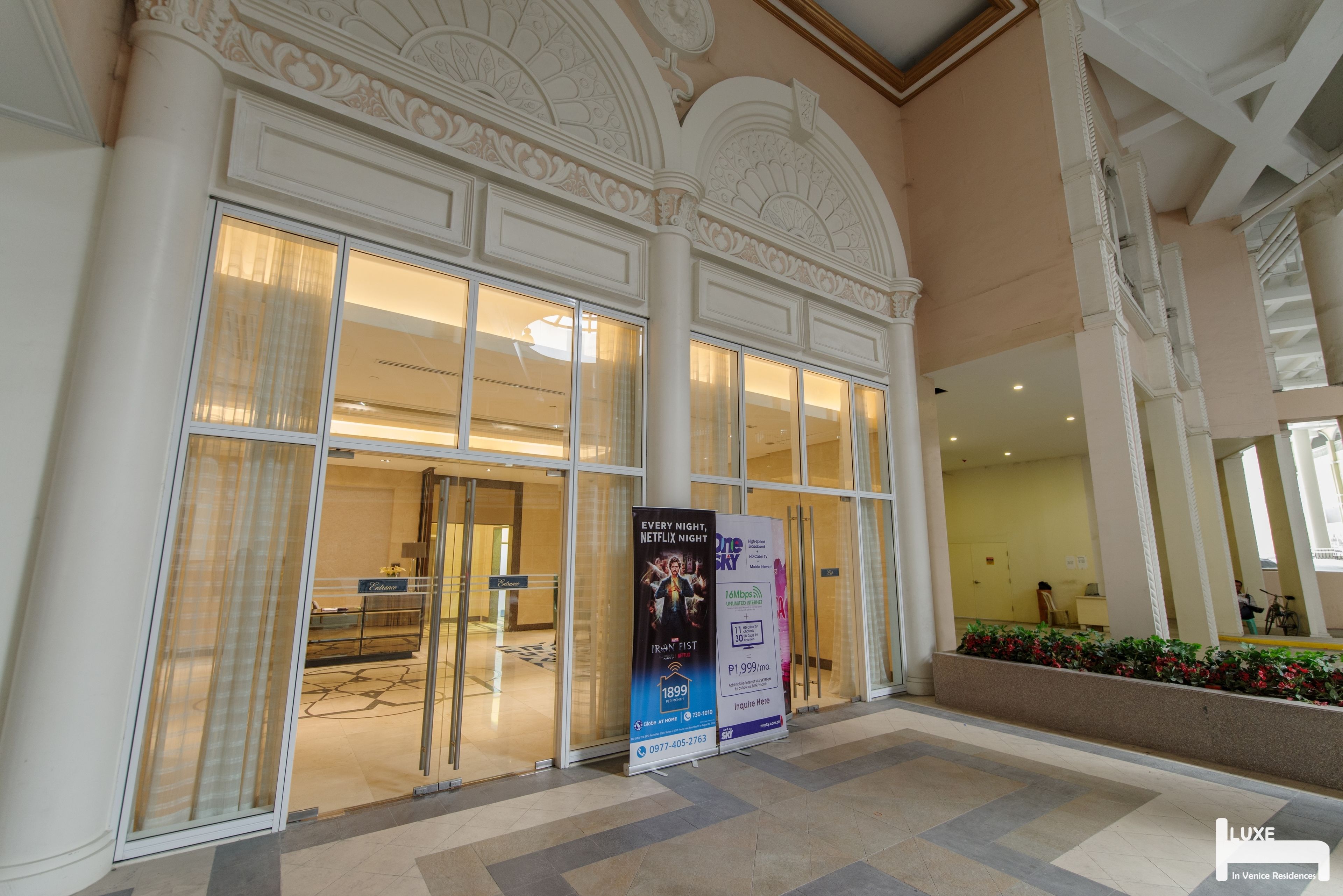 A hotel lobby with large glass doors, a decorative ceiling, and a sign advertising a Netflix night package.