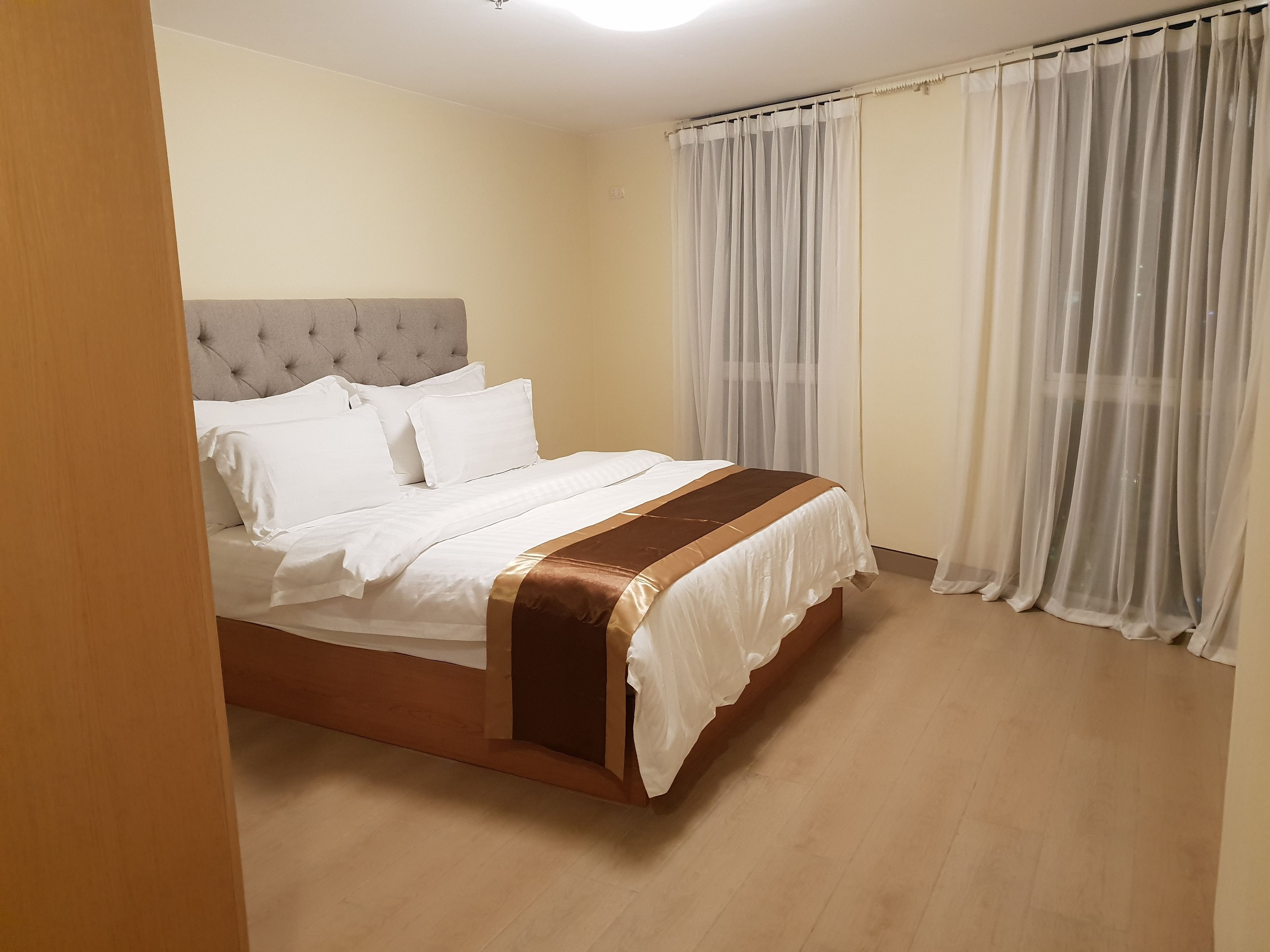 Ein ordentlich bezogenes Bett mit weißer und brauner Bettwäsche, einem karriertem Kopfteil und Holzboden.