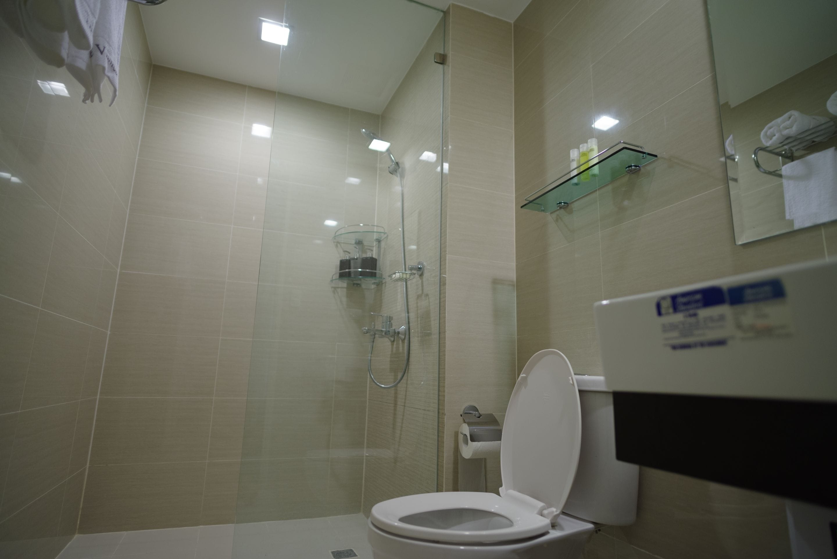 A modern bathroom with a glass-enclosed shower, a toilet, and a glass shelf with toiletries.