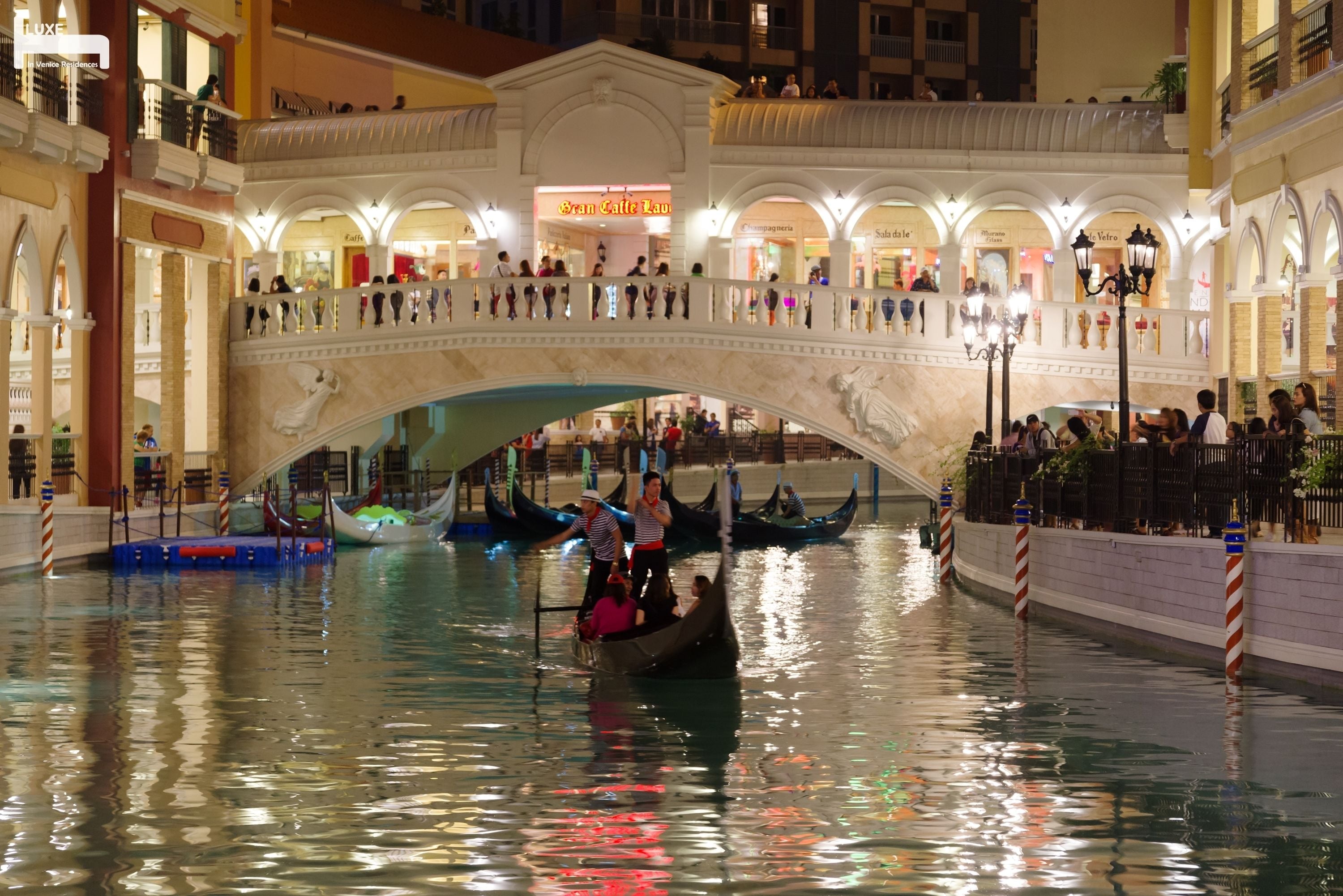 A canal with gondolas and a bridge with people on it.