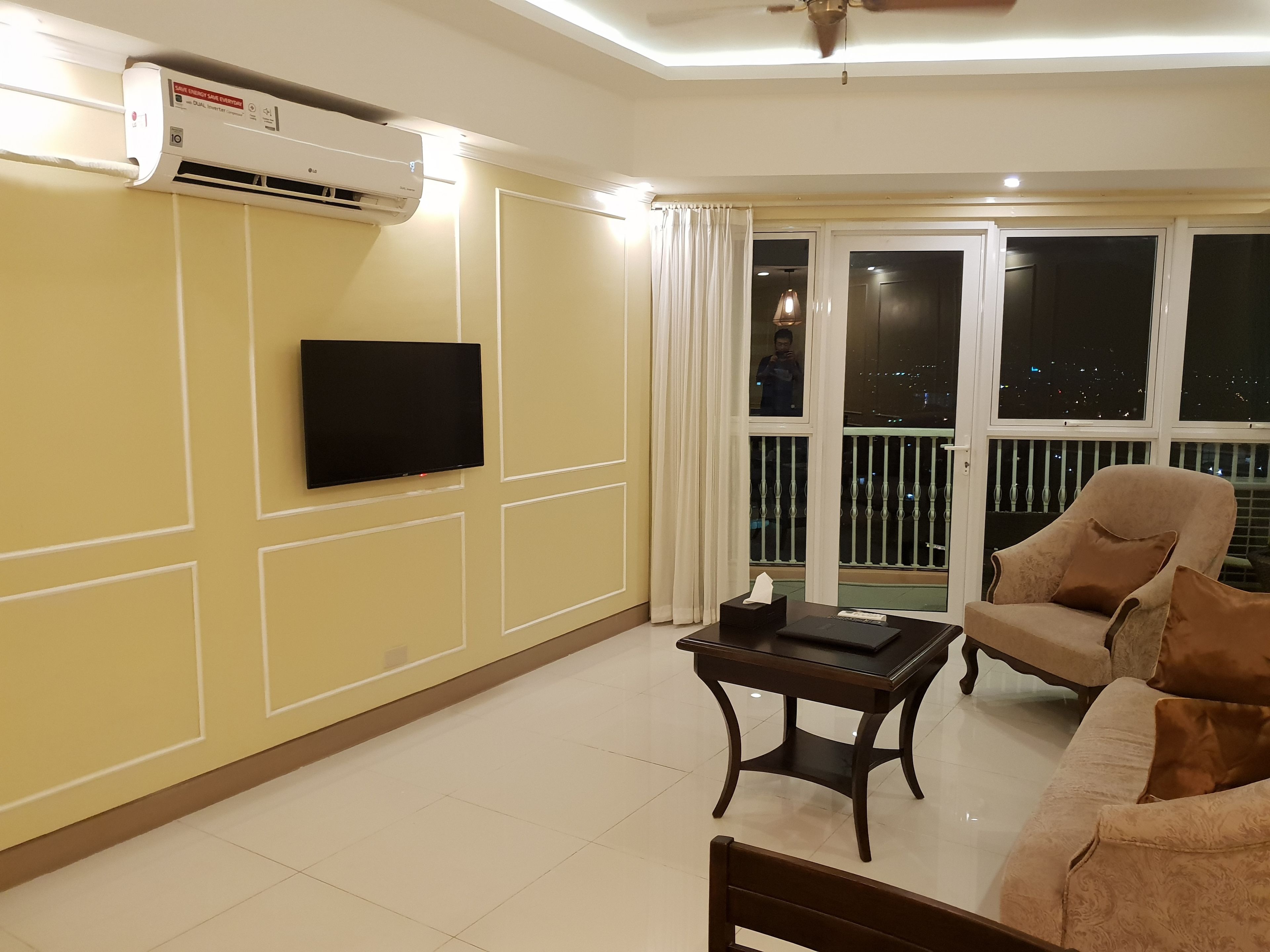 A living room with a flat-screen TV, a table with a tissue box, a sofa, and a balcony with a railing.