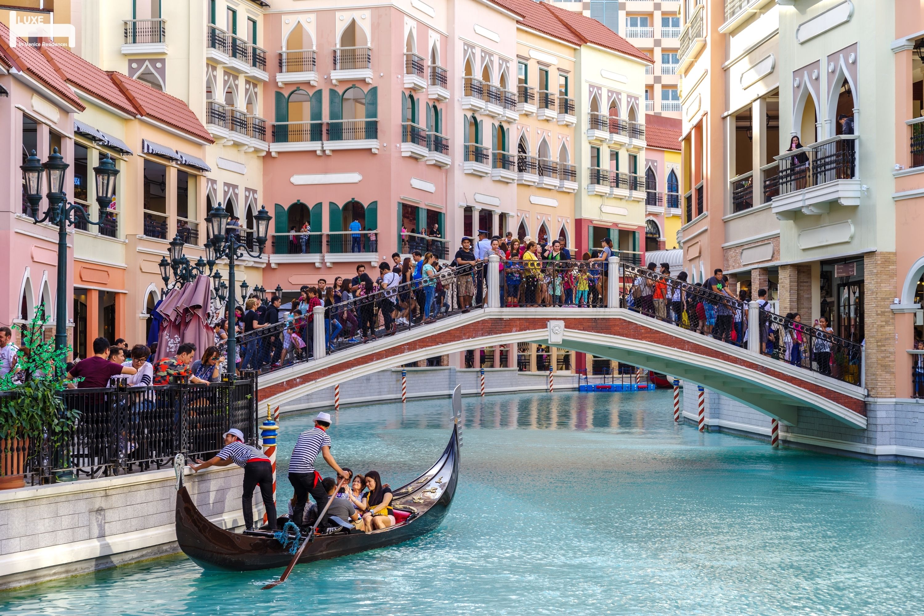 A gondola ride in a canal with a bridge and colorful buildings in the background.