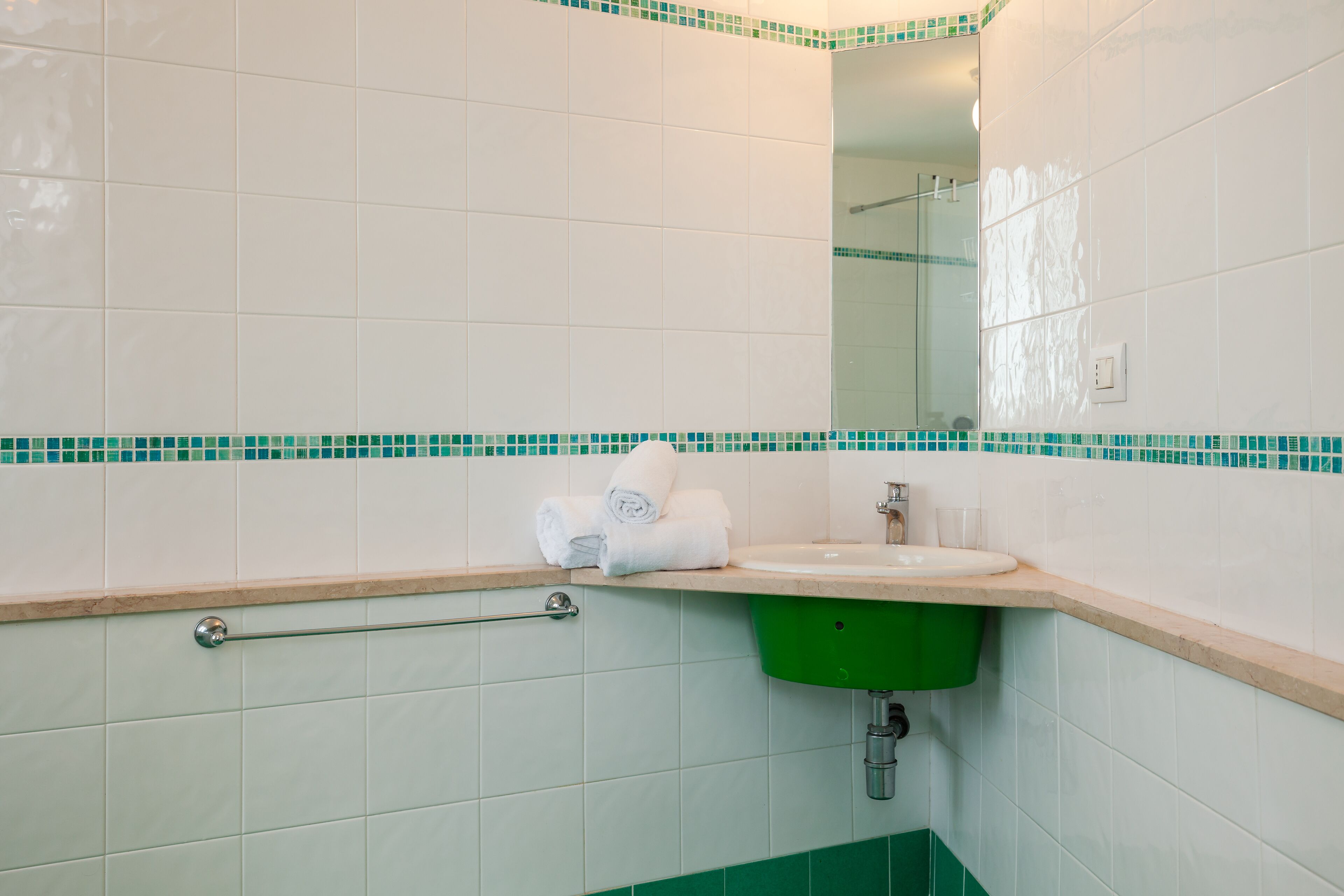 A bathroom with white tiles, a green sink, a towel rack, and a mirror.