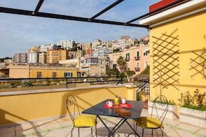 Ein Balkon mit Tisch und Stühlen, mit Blick auf eine dicht bebauete Stadtlandschaft mit verschiedenen Gebäuden.
