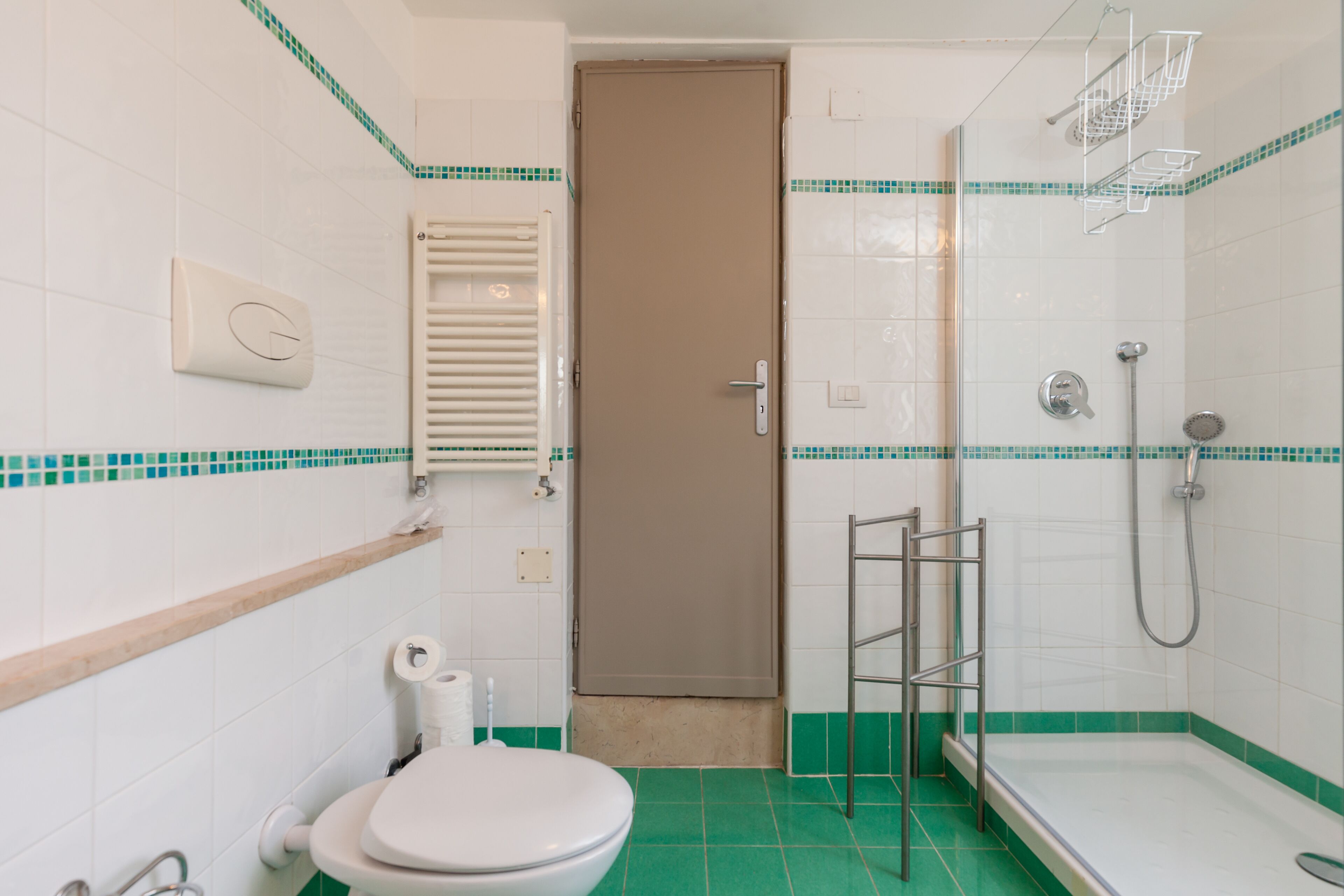 A bathroom with a toilet, sink, shower, and a door.