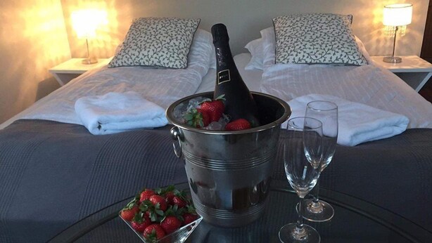 A bed with a metal bucket containing a bottle and strawberries, two glasses, and a tray of strawberries. - Hotel Eyjar (Vestmannaeyjar)
