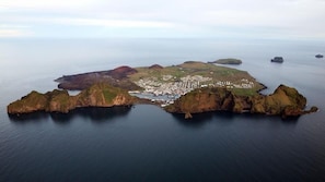 An aerial view of a coastal town with a harbor, surrounded by rocky outcrops and calm waters. - Hotel Eyjar (Vestmannaeyjar)
